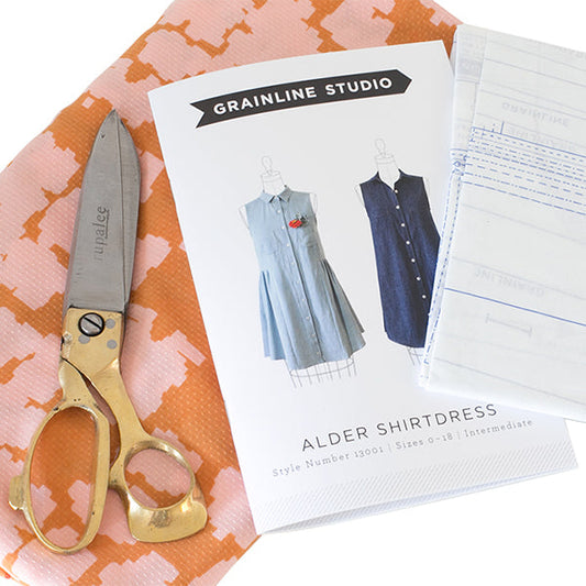 Grainline Studio Alder Shirtdress pattern envelope with both views, gold-handled scissors, and pink geometric print fabric