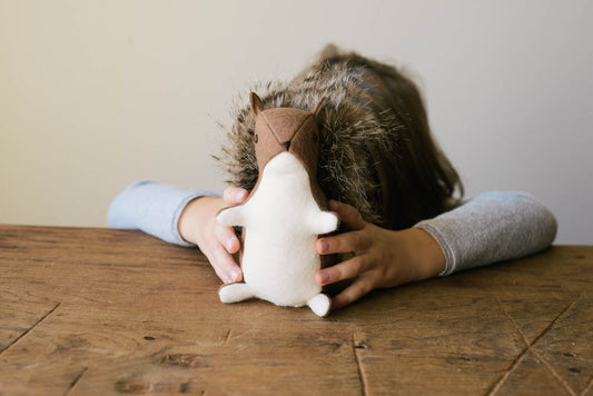 Child hugging a handmade Grainline Studio stuffed squirrel with tan felt ears and white plush body on a wooden table