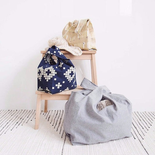 Three Stowe Bags in cream woven, navy geometric, and gray linen on a wooden step stool with yarn and patterned rug