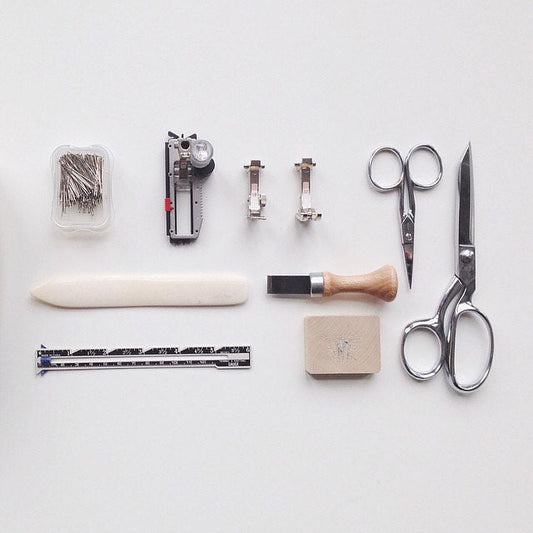 Flat lay of sewing tools: pins, presser feet, scissors, shears, bone folder, seam gauge, and buttonhole chisel