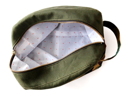 Portside Dopp Kit in olive and camouflage canvas, open to reveal white small-scale geometric print lining and gold zipper