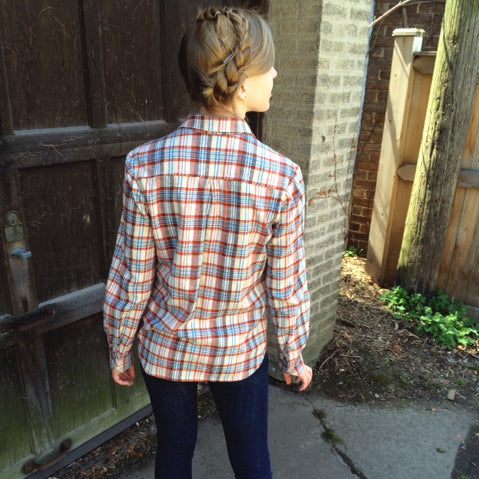 Archer Button Up in red, white, and blue plaid flannel, back view showing yoke detail, worn outdoors against brick wall