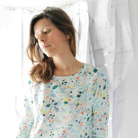 Person in a Linden Sweatshirt in light blue floral print French terry, standing beside hanging paper pattern pieces