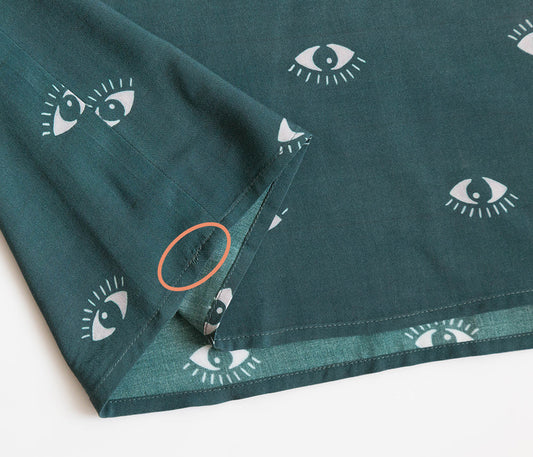 Scout Tee in teal with eye motif print showing backtack placement on shirt hem highlighted with orange circle annotation