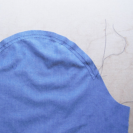 Close-up of a blue chambray Archer Button-Up sleeve cap with two rows of ease basting stitches on a work surface