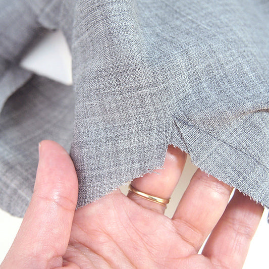 Close-up of hand holding gray stretch wool fabric edge to reveal serged seam allowance on a Morris Blazer sewing project