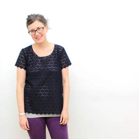 Person wearing a navy lace Scout Tee with scalloped hem over a gray underlayer, styled with purple pants