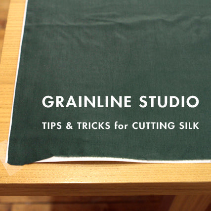 Green silk fabric on marker paper on a wooden table with text reading Grainline Studio Tips & Tricks for Cutting Silk