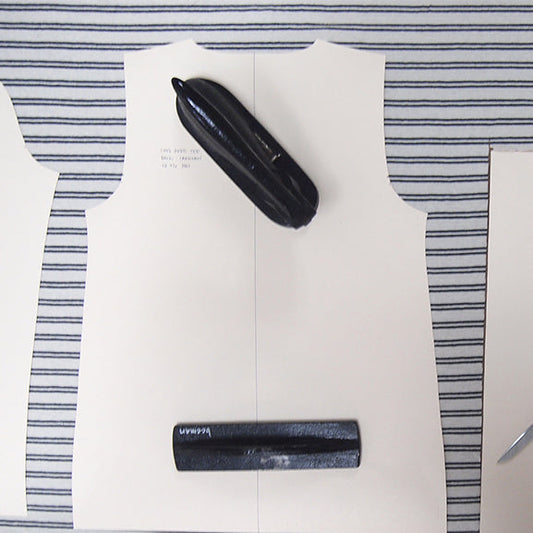 Lark Tee sewing pattern pieces laid on navy and white striped fabric with a pattern weight and pattern punch as weights