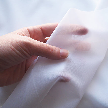 Hand holding white lightweight woven fusible interfacing, showing its semi-sheer drape and weight