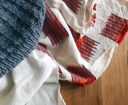 Blue handknit waffle sweater, white silk noil, and red and cream woven ikat fabric laid on a wooden surface