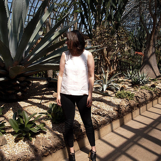 Person wearing white sleeveless Willow Tank in a sunny conservatory surrounded by desert plants and large agave leaves