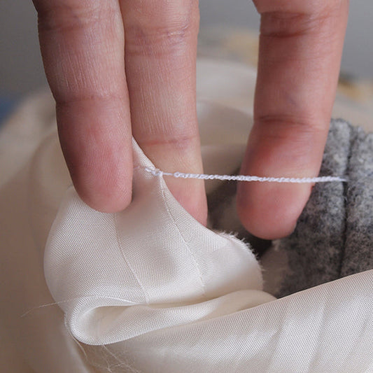 Close-up of hands demonstrating a thread chain, connecting white lining to gray wool with a hand-crocheted thread chain