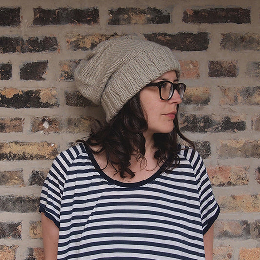 Person wearing cream ribbed knit beanie and Penny Raglan in navy and white stripes, standing against brick wall