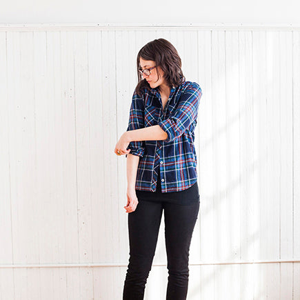 Archer Button Up Shirt in blue plaid flannel with black pants, worn with sleeves rolled and cuffs unbuttoned