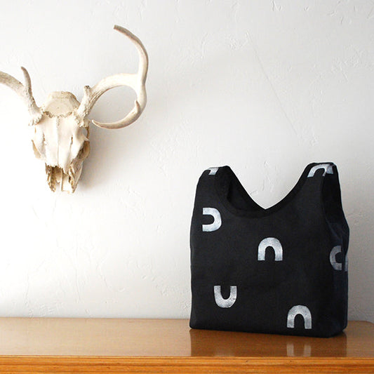 Stowe Bag in black fabric with white block-printed horseshoe motifs, on a wooden surface beside a bleached animal skull