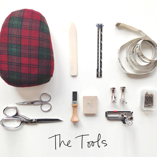 Flat lay of Alder Shirtdress sew-along tools: tartan pressing ham, scissors, tailor's chalk, buttonhole chisel, and pins