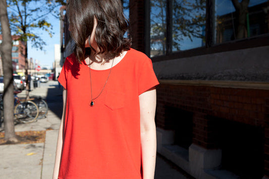 Person wearing red wool crepe Scout Tee with modified fuller back and chest pocket, standing on urban sidewalk