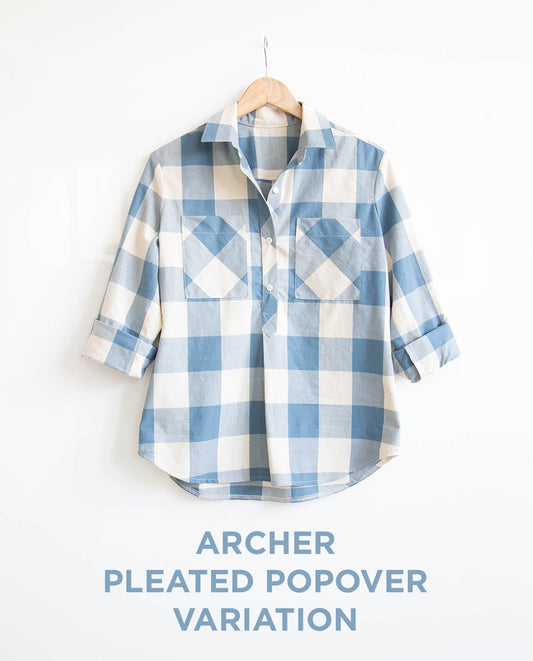 Archer Pleated Popover variation in blue and white buffalo plaid with patch pockets and rolled sleeves on a wooden hanger