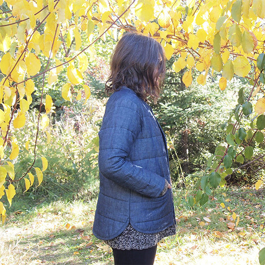 Woman wearing blue plaid quilted Tamarack Jacket with horizontal quilting lines, standing under yellow autumn foliage