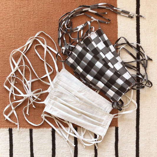 Homemade fabric face masks in white and black-and-white gingham with fabric ties, on striped woven fabric
