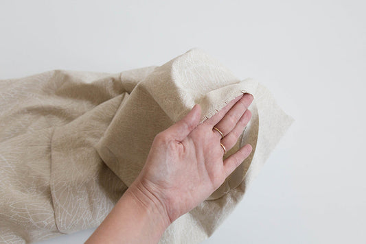 Hand holding cream linen fabric showing flat bias facing sewn to neckline edge with visible whip stitch on Willow Tank