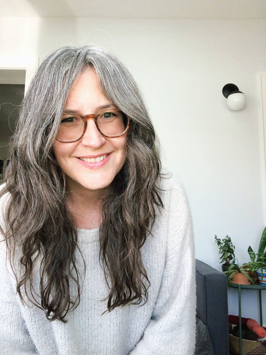Person wearing hand-knit white Addison Sweater by Julie Hoover in Woolfolk Flette yarn, smiling indoors near houseplants