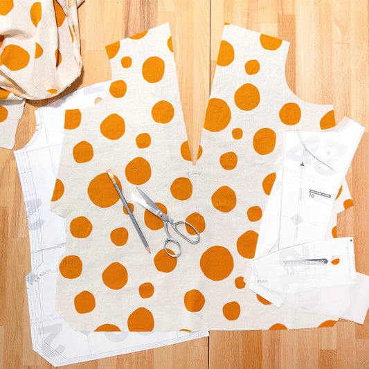 Augusta Shirt & Dress cutting layout in cream linen with orange polka dots, with paper pattern pieces, scissors, and pencil