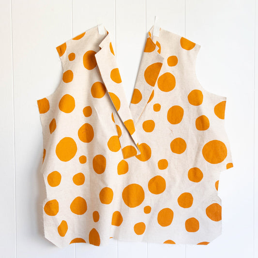 Augusta Shirt & Dress in cream linen with orange polka dots, showing lapel assembly taped flat against a white wall