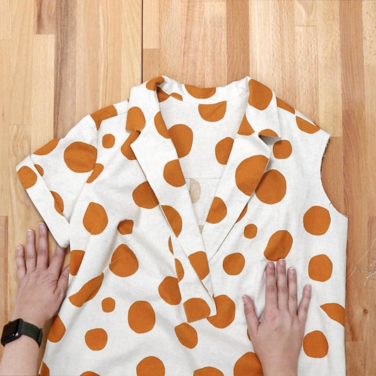 Augusta Shirt & Dress in cream linen with orange polka dots, showing sleeve and collar construction, hands flat on wood table