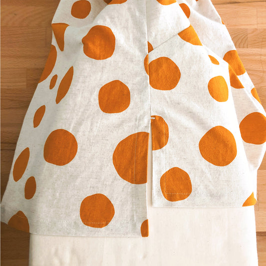 Augusta Shirt & Dress in cream linen with orange polka dot print, showing mitered hem construction detail on wooden table