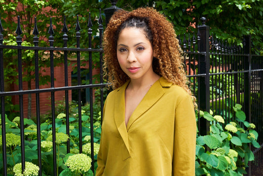 Woman wearing mustard rayon Augusta Shirt & Dress with asymmetrical collar, in front of black iron fence with green foliage