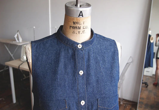 Sleeveless Alder Shirtdress in dark denim on a dress form, featuring a band collar and white buttons