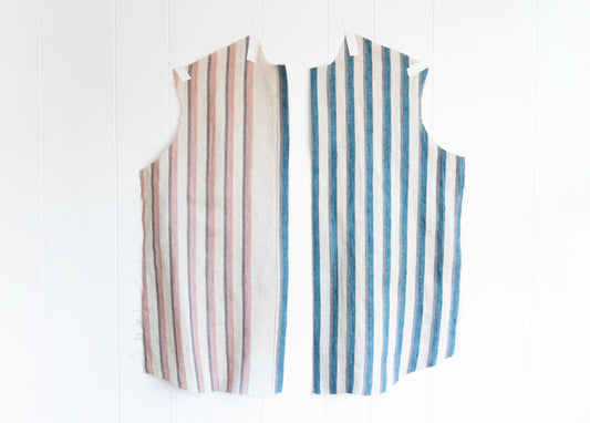 Two Archer Button Up front pattern pieces in vertical striped linen, pink and blue colorways, taped to a white wall