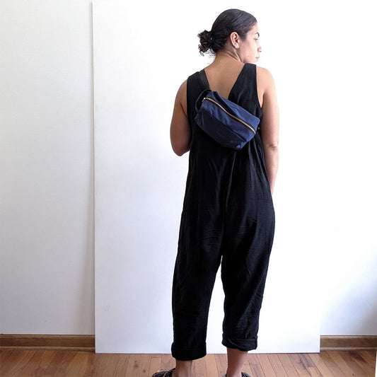 Back view of dark indigo sleeveless jumpsuit, styled with hacked navy Portside Dopp Kit worn as a crossbody bag