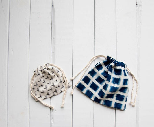 Two ikat drawstring pouches on a white wood surface: small cream and gray, large navy and white grid, with cotton string