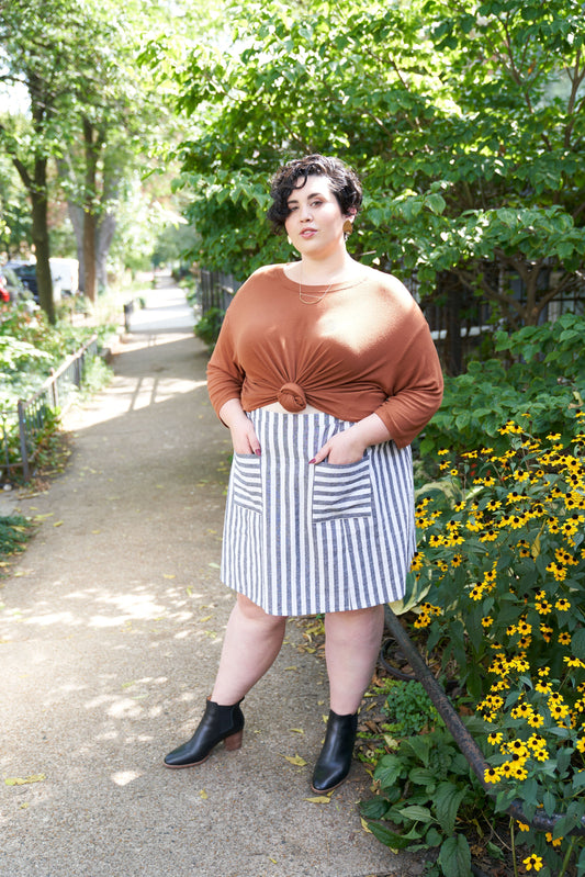 Rust Hemlock Tee with knotted front hem and gray-white striped linen blend Reed Skirt on Chicago sidewalk with flowers