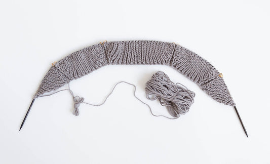 Gray fisherman's rib knit sweater in progress on circular needles with stitch markers, part of Fringe and Friends KAL
