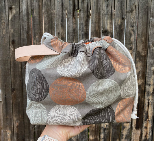 Field Bag in gray, cream, and rust yarn ball print fabric with cream canvas handle, held against weathered wood fence