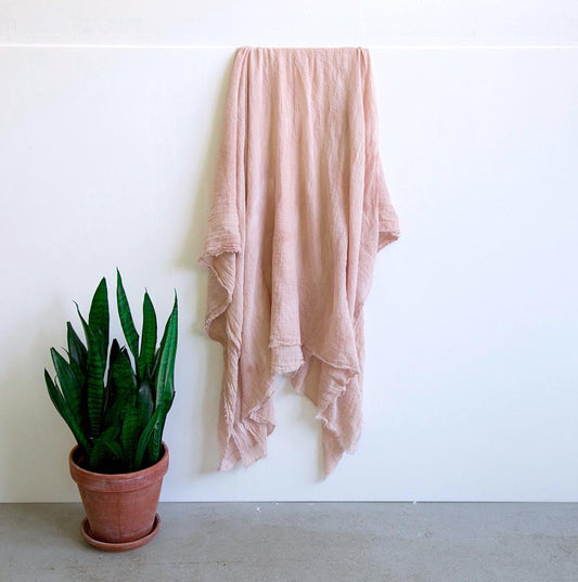 Dusty rose naturally dyed cotton gauze with avocado pits, draped on a white wall next to a potted snake plant