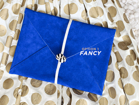 Cobalt leather envelope clutch with white strap and button clasp on cream and gold polka dot fabric, labeled 'Option 1 Fancy