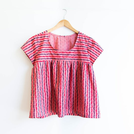 Scout Tee in pink and navy abstract stripe with gathered bodice below contrast horizontal stripe yoke, on wooden hanger