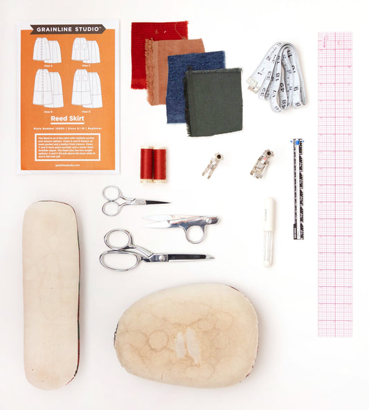 Reed Skirt pattern envelope with supplies: fabric swatches, red thread, scissors, zipper feet, tape measure, and pressing ham