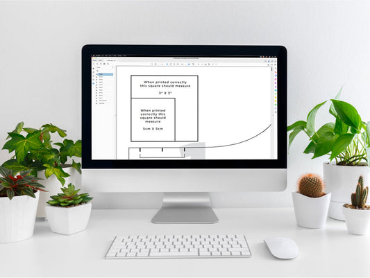 iMac displaying Hadley Top layered PDF pattern with print calibration squares, surrounded by potted plants and succulents