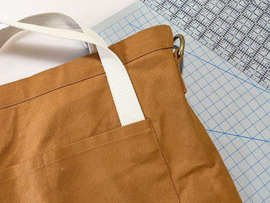 Hacked Town Bag in toffee canvas with natural cotton webbing handles and brass ring, on cutting mat with gridded ruler