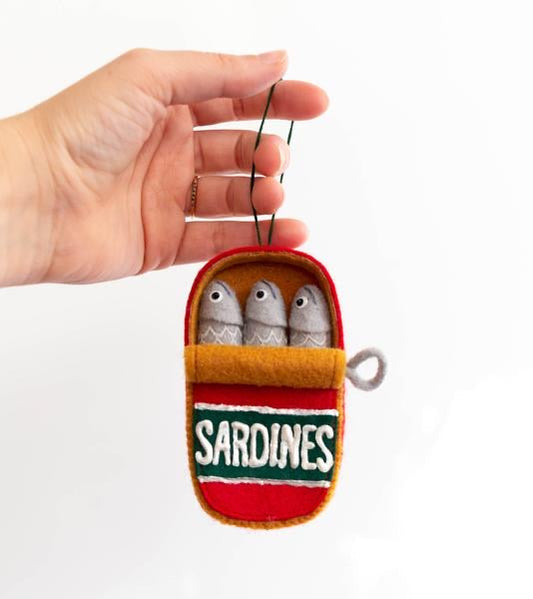 Grainline Can of Sardines Ornament: red and orange felt can with three gray felt fish, held by hand, on white