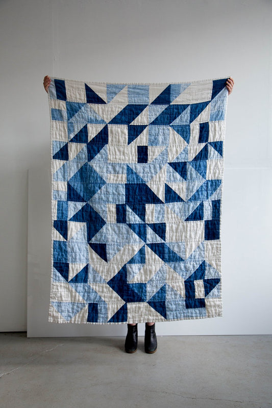 Person holding up a large indigo and cream geometric quilt made from navy and light blue denim half-square triangles