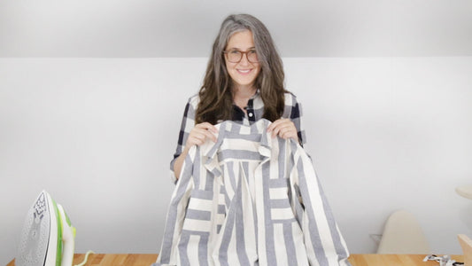 Person wearing navy gingham Archer Button Up, holding up gray striped Archer shirt during collar assembly and attachment step