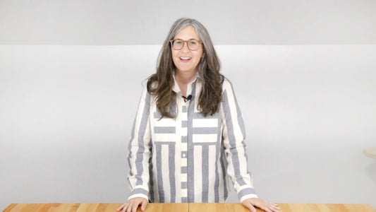 Person wearing completed gray and white striped Archer Button Up, standing at wood table for the final day of the sew-along