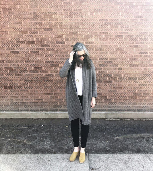 Hand-knit charcoal Parker Cardigan by Julie Hoover, worn over white Hadley Top, black jeans, and lichen Bryr clogs